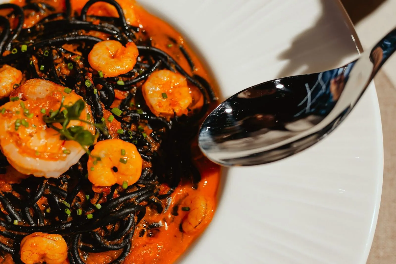 A plate of black pasta with prawns, spoon above the plate